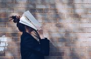 A woman covering her face with a book.